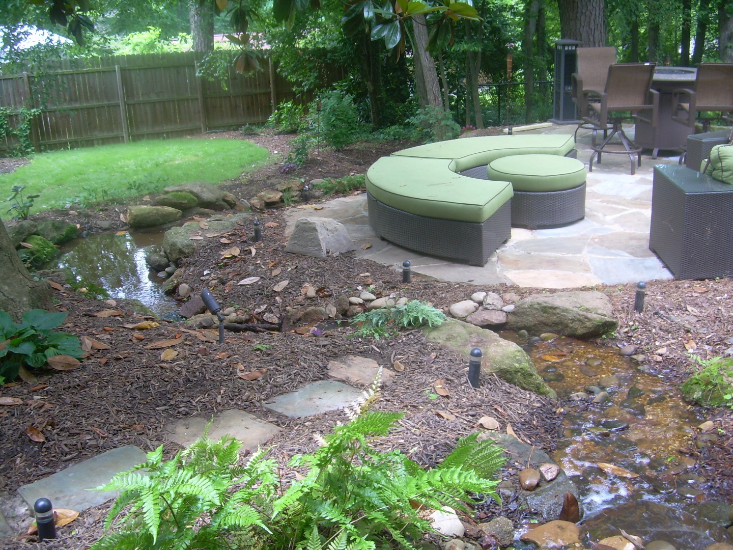 A shaded garden stream winding around a natural-stone patio